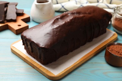 Photo of Tasty chocolate sponge cake and cocoa powder on light blue wooden table, closeup