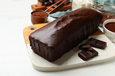 Photo of Tasty sponge cake, pieces of chocolate and cocoa powder on white table, closeup