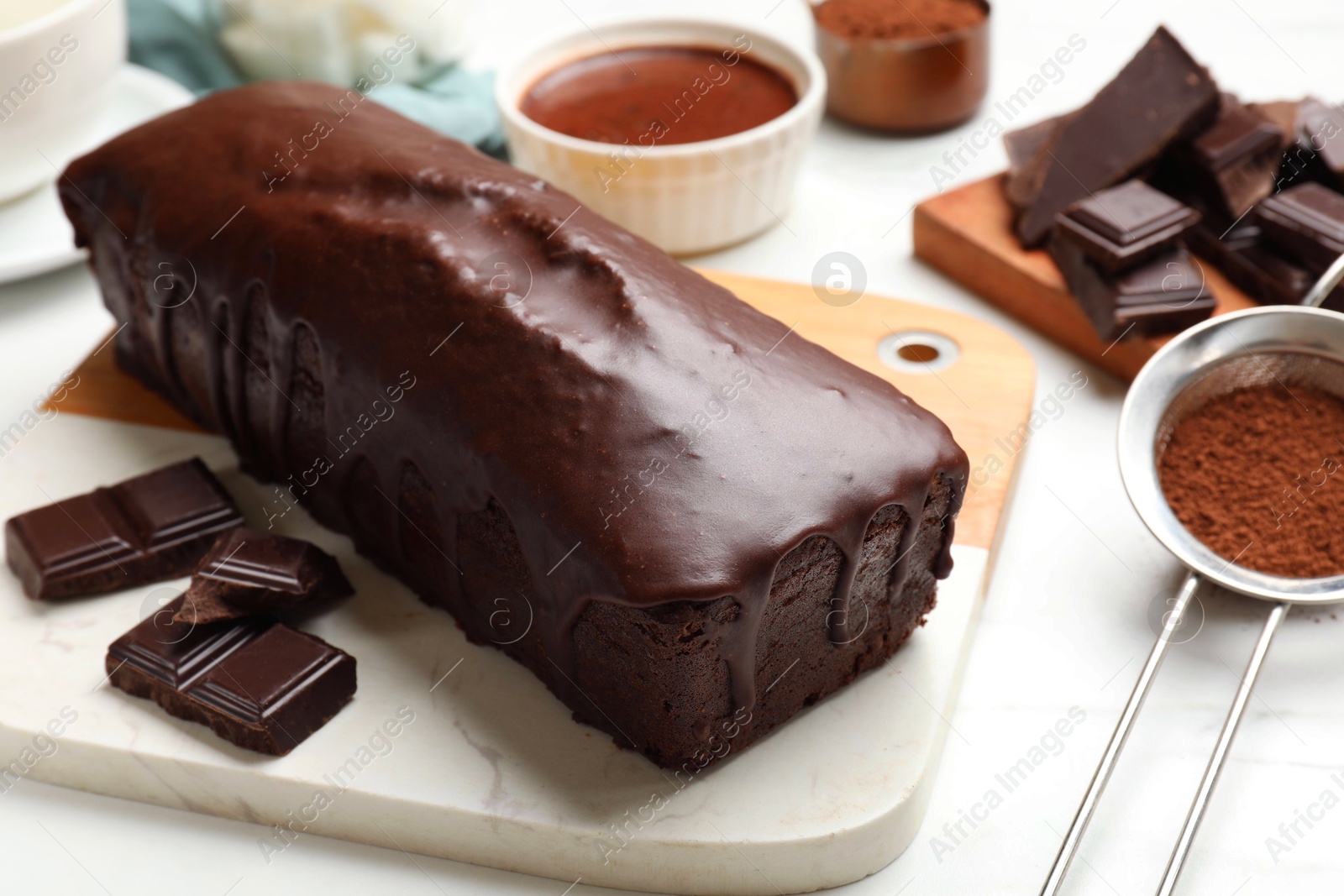 Photo of Tasty sponge cake, pieces of chocolate and cocoa powder on white table, closeup