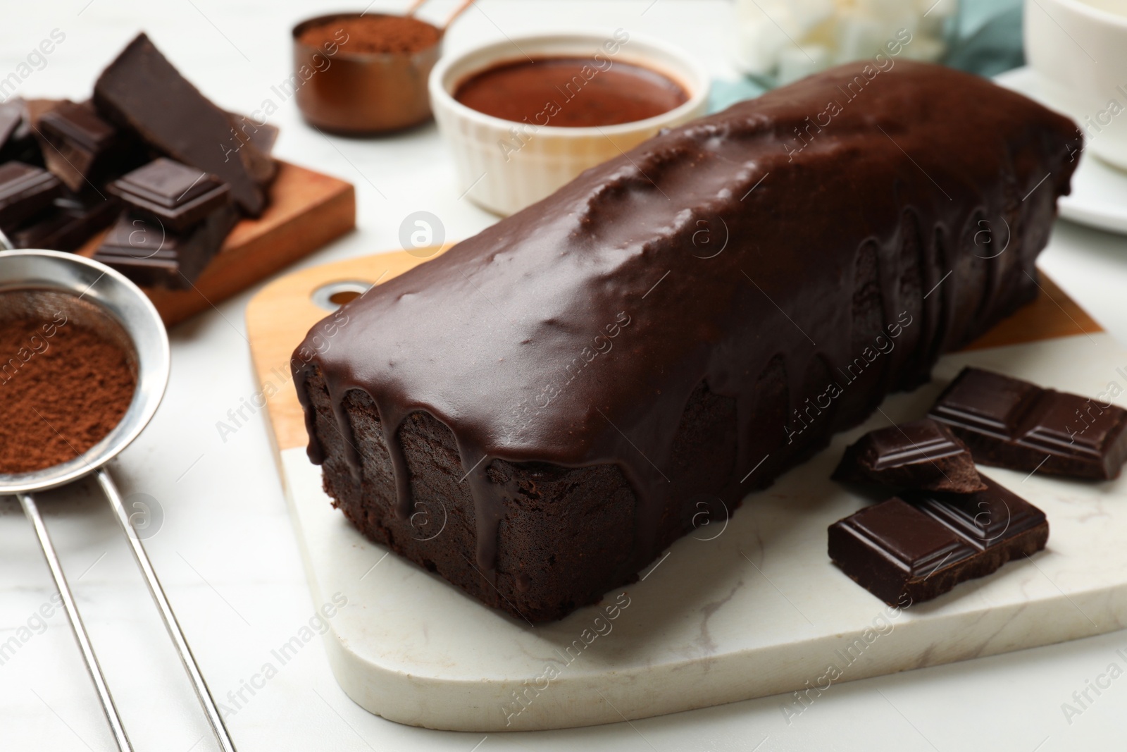 Photo of Tasty sponge cake, pieces of chocolate and cocoa powder on white table, closeup