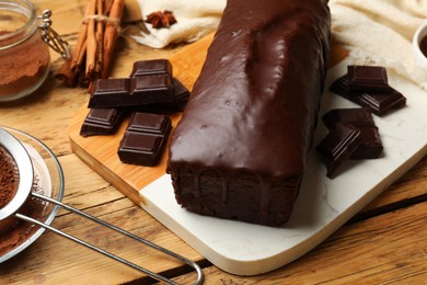 Photo of Tasty sponge cake and pieces of chocolate on wooden table, closeup