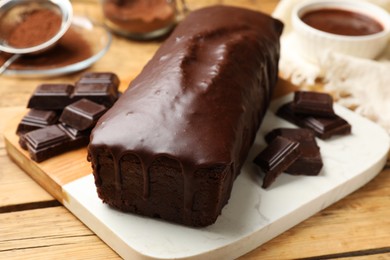 Photo of Tasty sponge cake and pieces of chocolate on wooden table, closeup