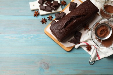 Photo of Tasty chocolate sponge cake and ingredients on light blue wooden table, top view. Space for text