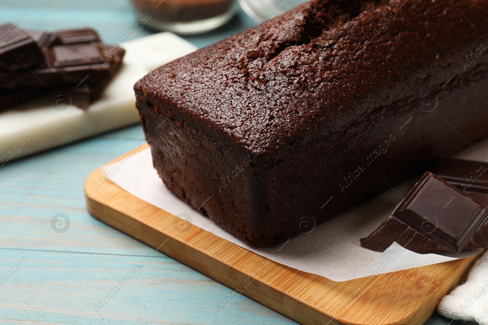 Photo of Tasty sponge cake and pieces of chocolate on light blue wooden background, closeup