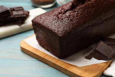 Photo of Tasty sponge cake and pieces of chocolate on light blue wooden background, closeup