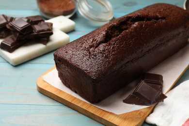 Photo of Tasty sponge cake and pieces of chocolate on light blue wooden background, closeup