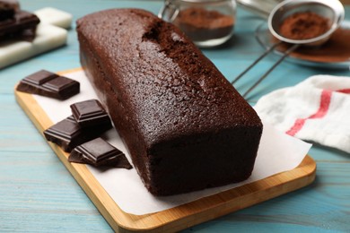 Photo of Tasty sponge cake and pieces of chocolate on light blue wooden background, closeup