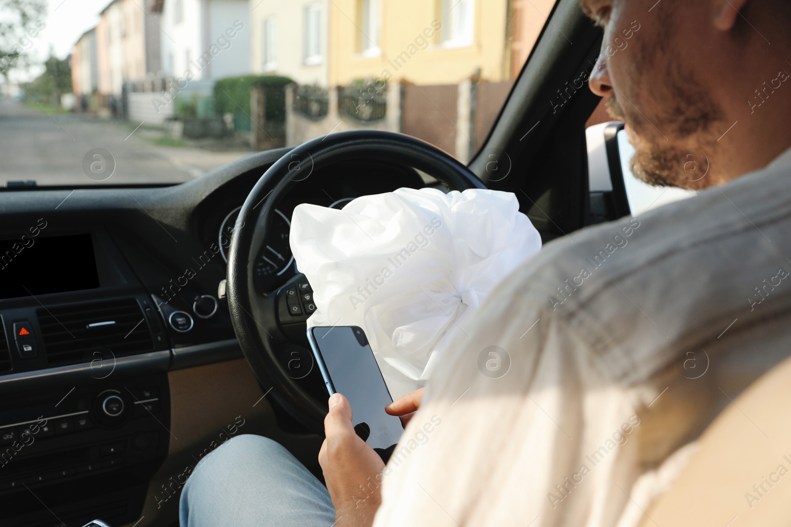 Photo of Man using smartphone near opened airbag in automobile after car accident, closeup