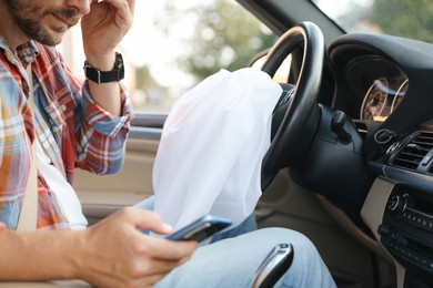 Photo of Man using smartphone near opened airbag in automobile after car accident, closeup