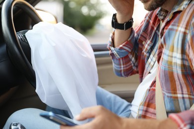 Photo of Man using smartphone near opened airbag in automobile after car accident, closeup