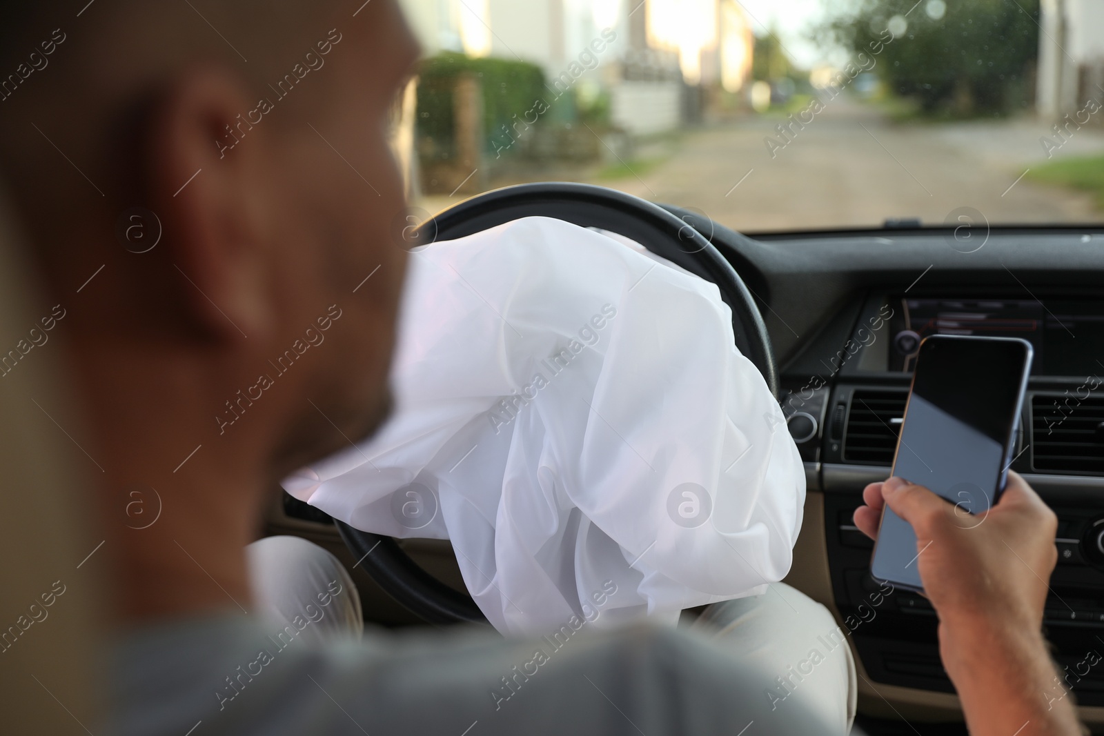 Photo of Man using smartphone near opened airbag in automobile after car accident, closeup