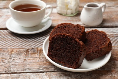 Photo of Slices of delicious chocolate sponge cake and tea on wooden table, closeup