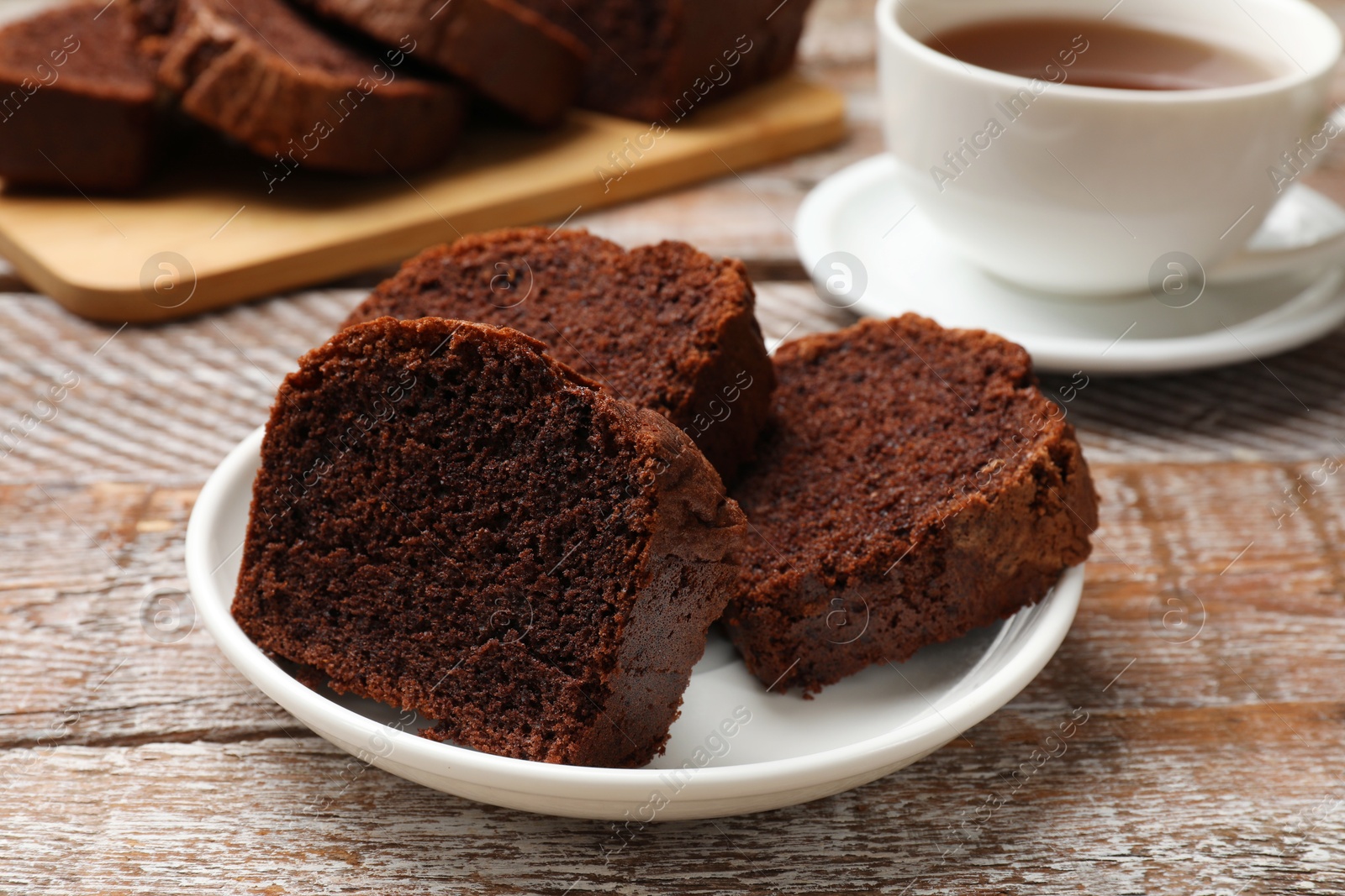 Photo of Slices of delicious chocolate sponge cake and tea on wooden table, closeup