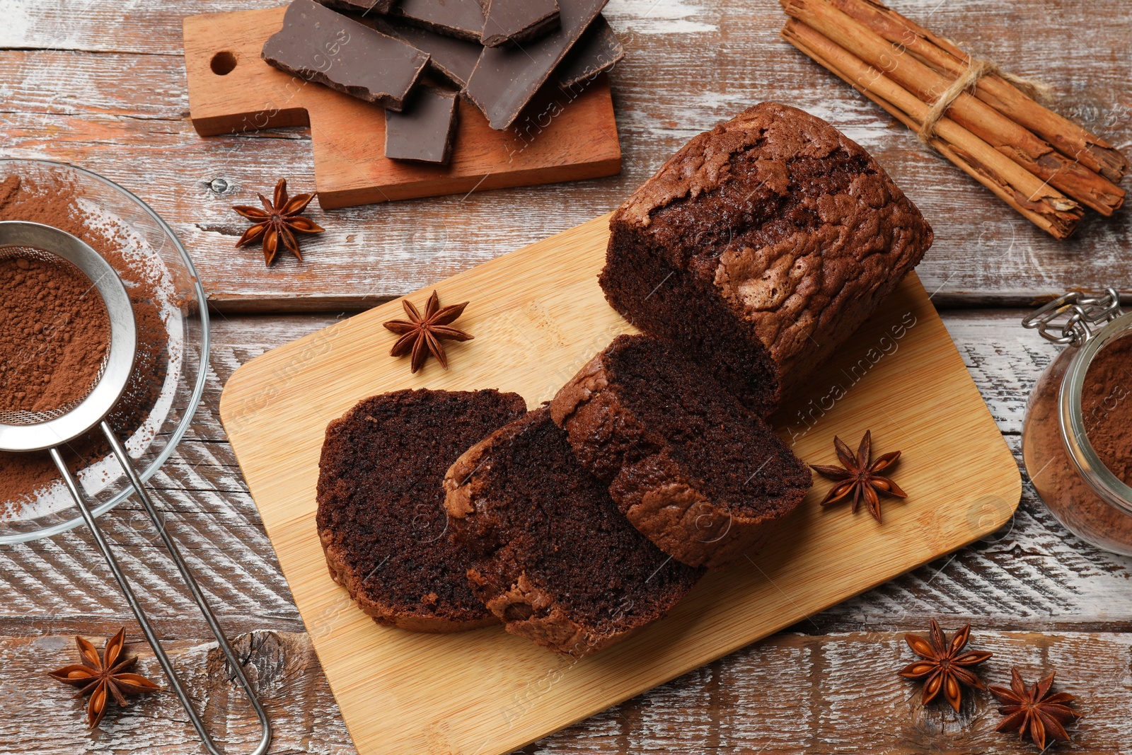 Photo of Delicious cut chocolate sponge cake and ingredients on wooden table, flat lay