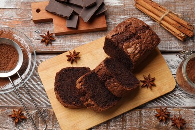 Photo of Delicious cut chocolate sponge cake and ingredients on wooden table, flat lay