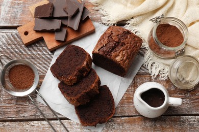 Photo of Delicious cut chocolate sponge cake and ingredients on wooden table, flat lay