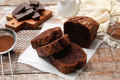 Photo of Delicious cut chocolate sponge cake and ingredients on wooden table, closeup