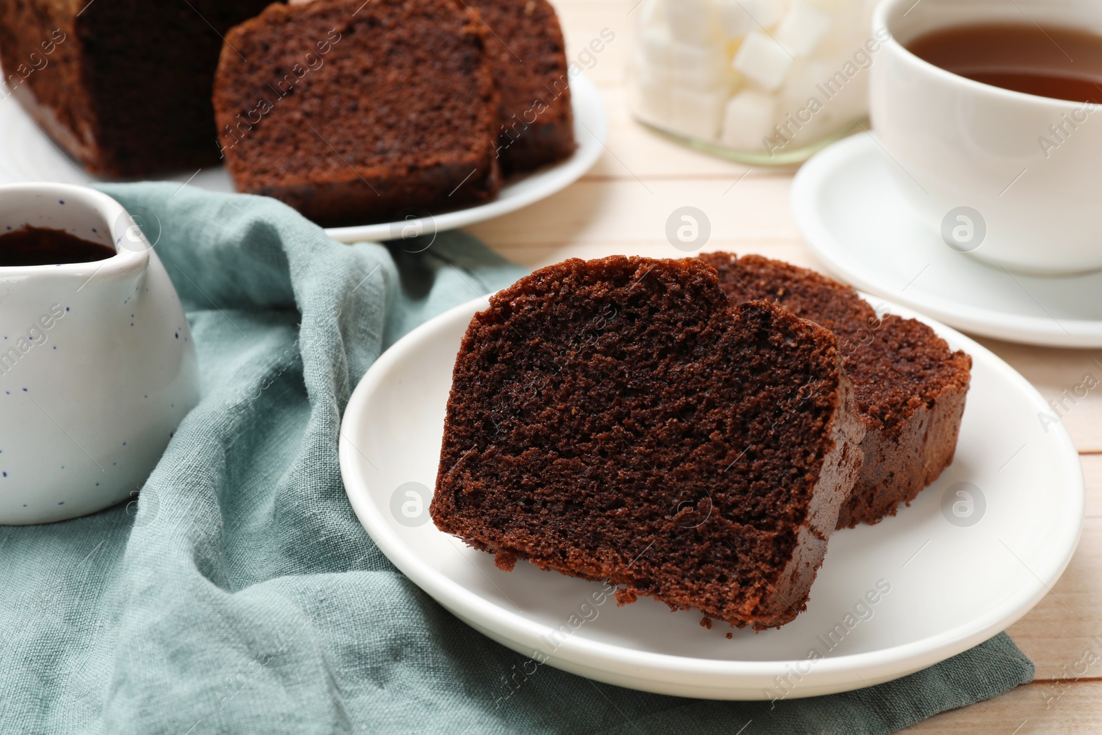 Photo of Slices of delicious chocolate sponge cake and tea on white wooden table, closeup