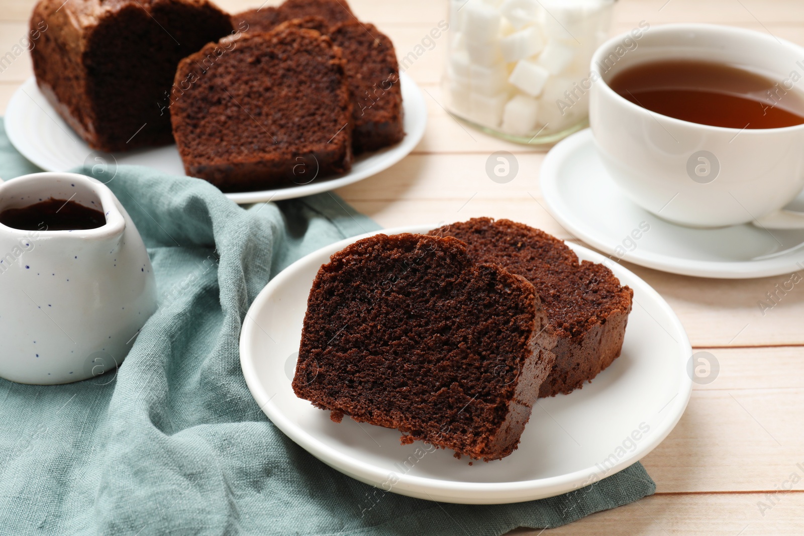 Photo of Slices of delicious chocolate sponge cake and tea on white wooden table