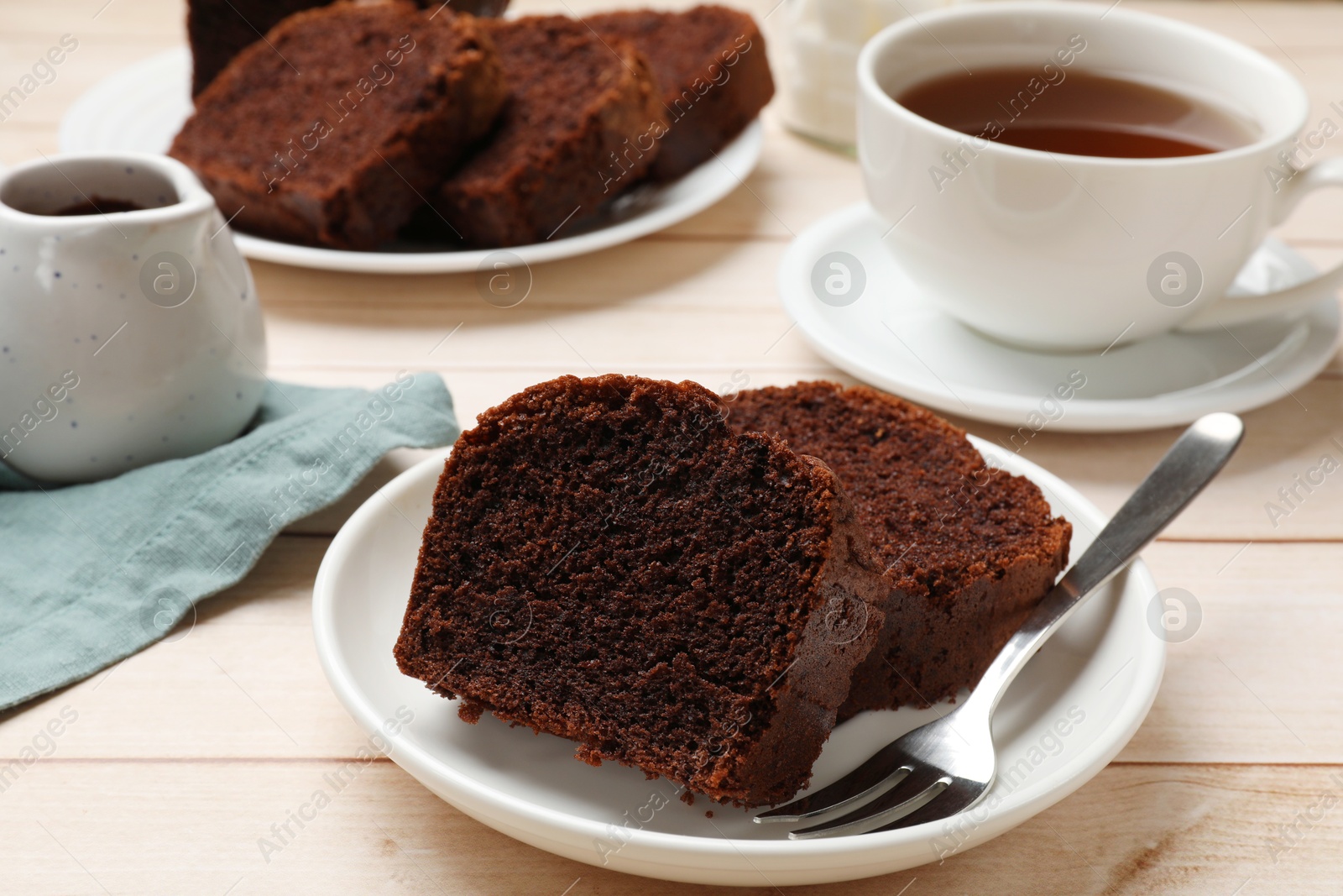 Photo of Slices of delicious chocolate sponge cake and tea on white wooden table, closeup