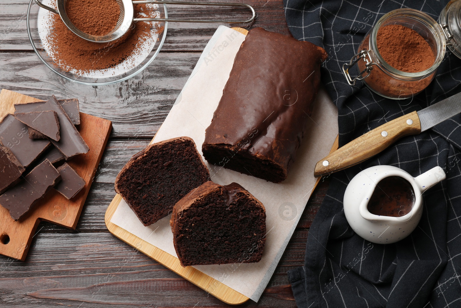 Photo of Delicious cut chocolate sponge cake and ingredients on wooden table, flat lay