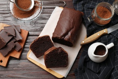 Photo of Delicious cut chocolate sponge cake and ingredients on wooden table, flat lay