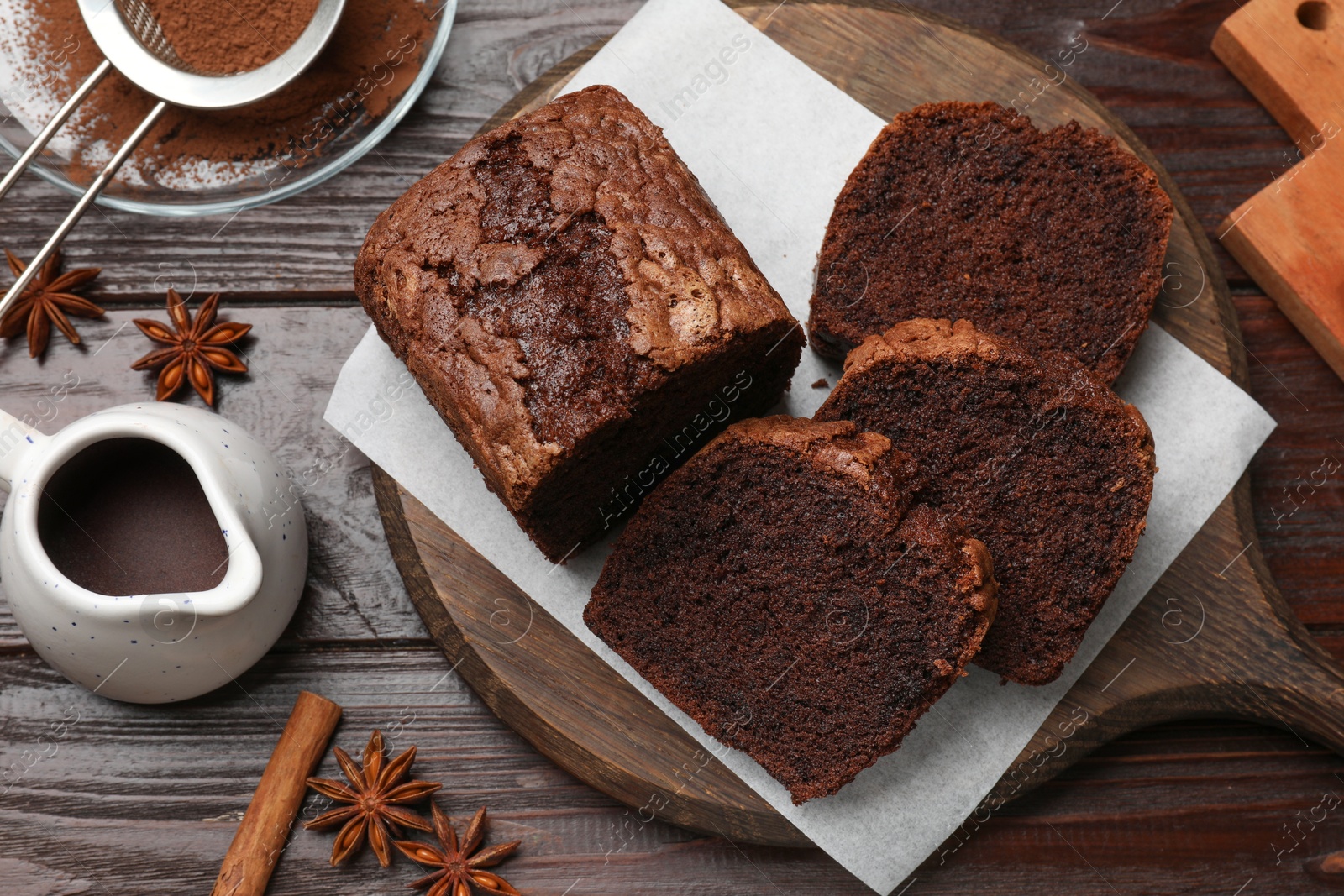 Photo of Delicious cut chocolate sponge cake and ingredients on wooden table, flat lay