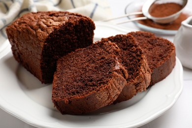 Photo of Delicious cut chocolate sponge cake on white tiled table, closeup