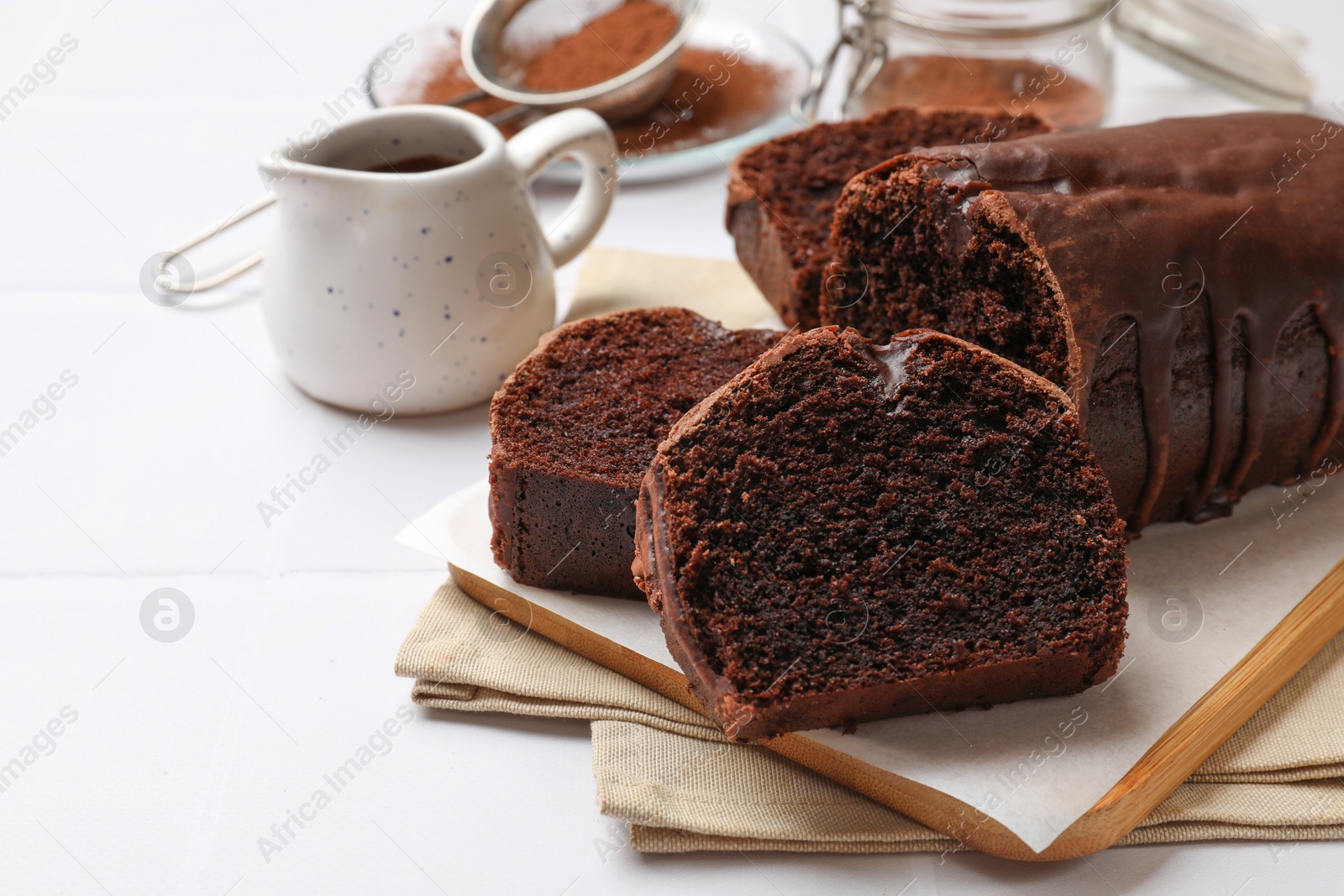 Photo of Delicious cut chocolate sponge cake on white tiled table, closeup