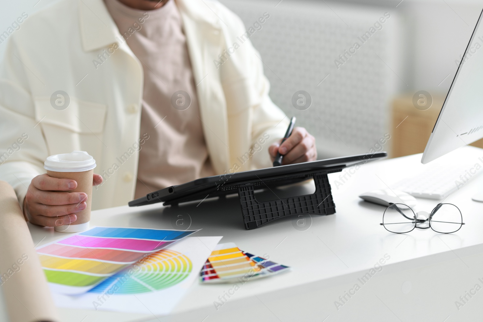 Photo of Designer with paper cup of drink working on tablet at table in office, closeup