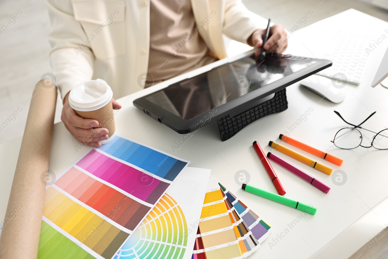 Photo of Designer with paper cup of drink using tablet at table in office, closeup