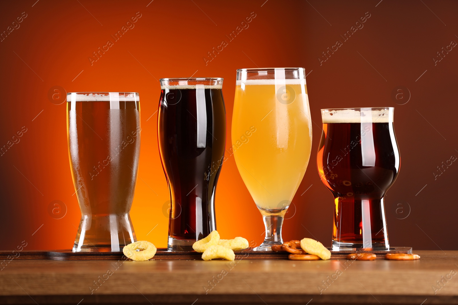 Photo of Glasses with different types of beer on wooden table against color background