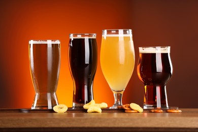 Photo of Glasses with different types of beer on wooden table against color background