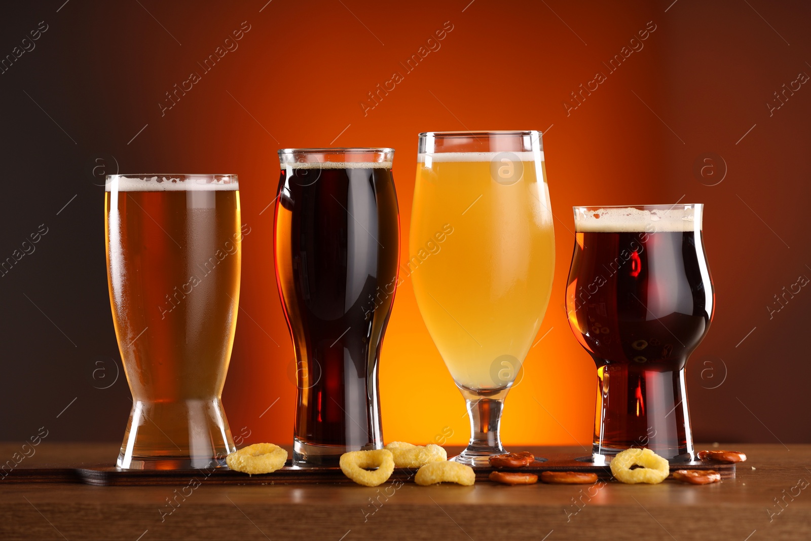 Photo of Glasses with different types of beer on wooden table against color background