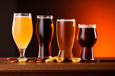 Photo of Glasses with different types of beer on wooden table against color background