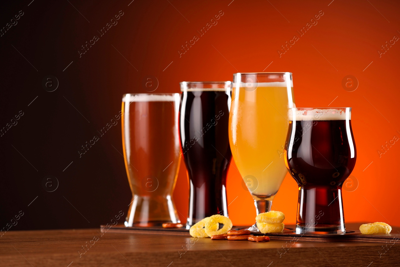 Photo of Glasses with different types of beer on wooden table against color background