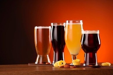 Photo of Glasses with different types of beer on wooden table against color background