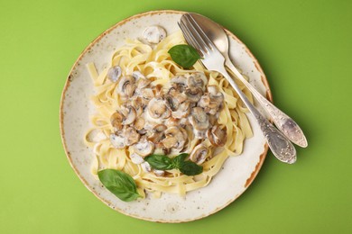 Photo of Delicious pasta with mushrooms and basil served on light green background, top view