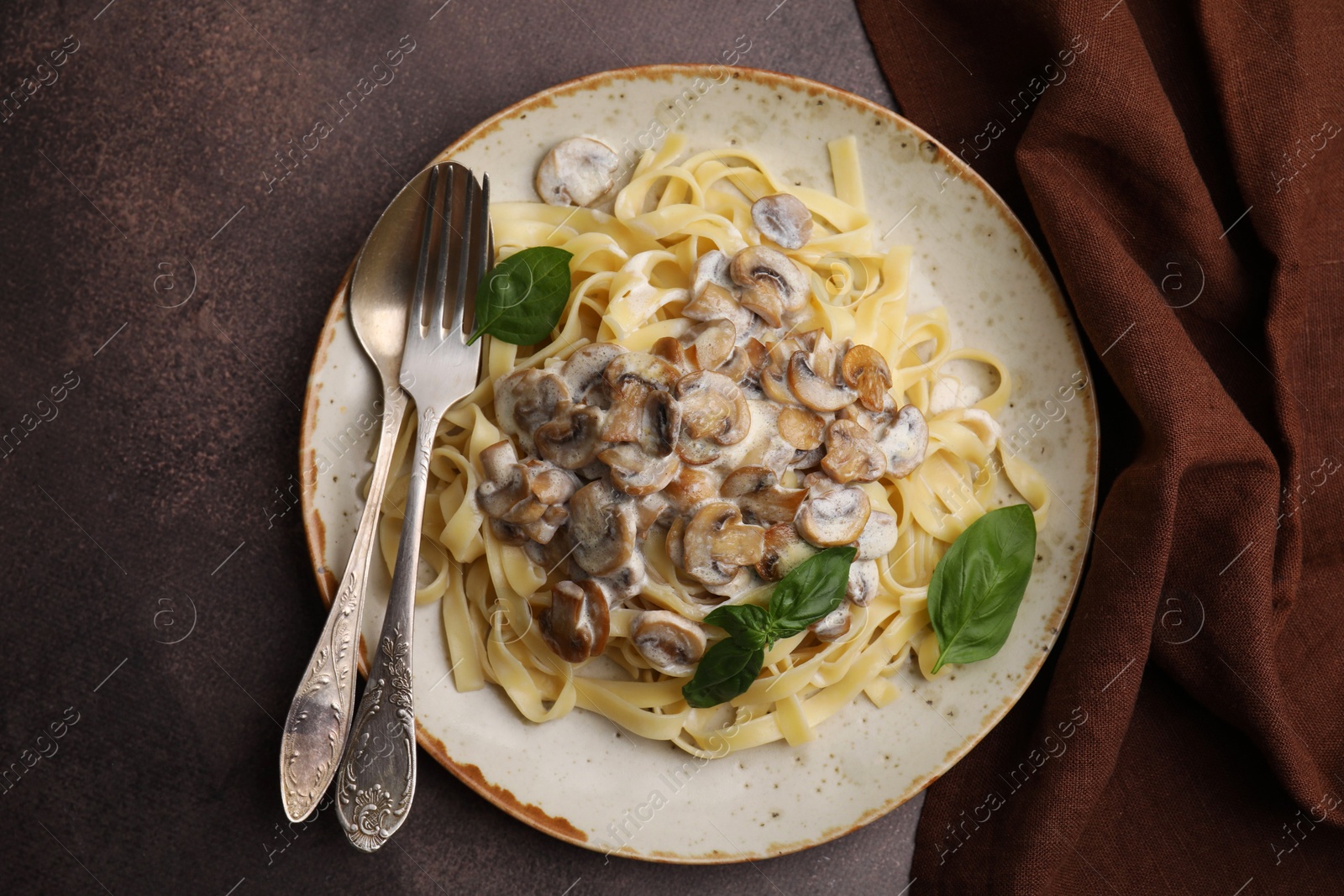 Photo of Delicious pasta with mushrooms and basil served on brown table, top view