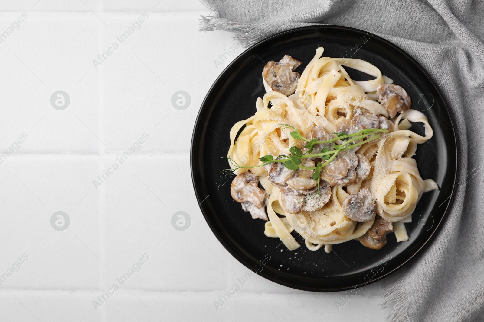 Photo of Delicious pasta with mushrooms on white tiled table, top view. Space for text