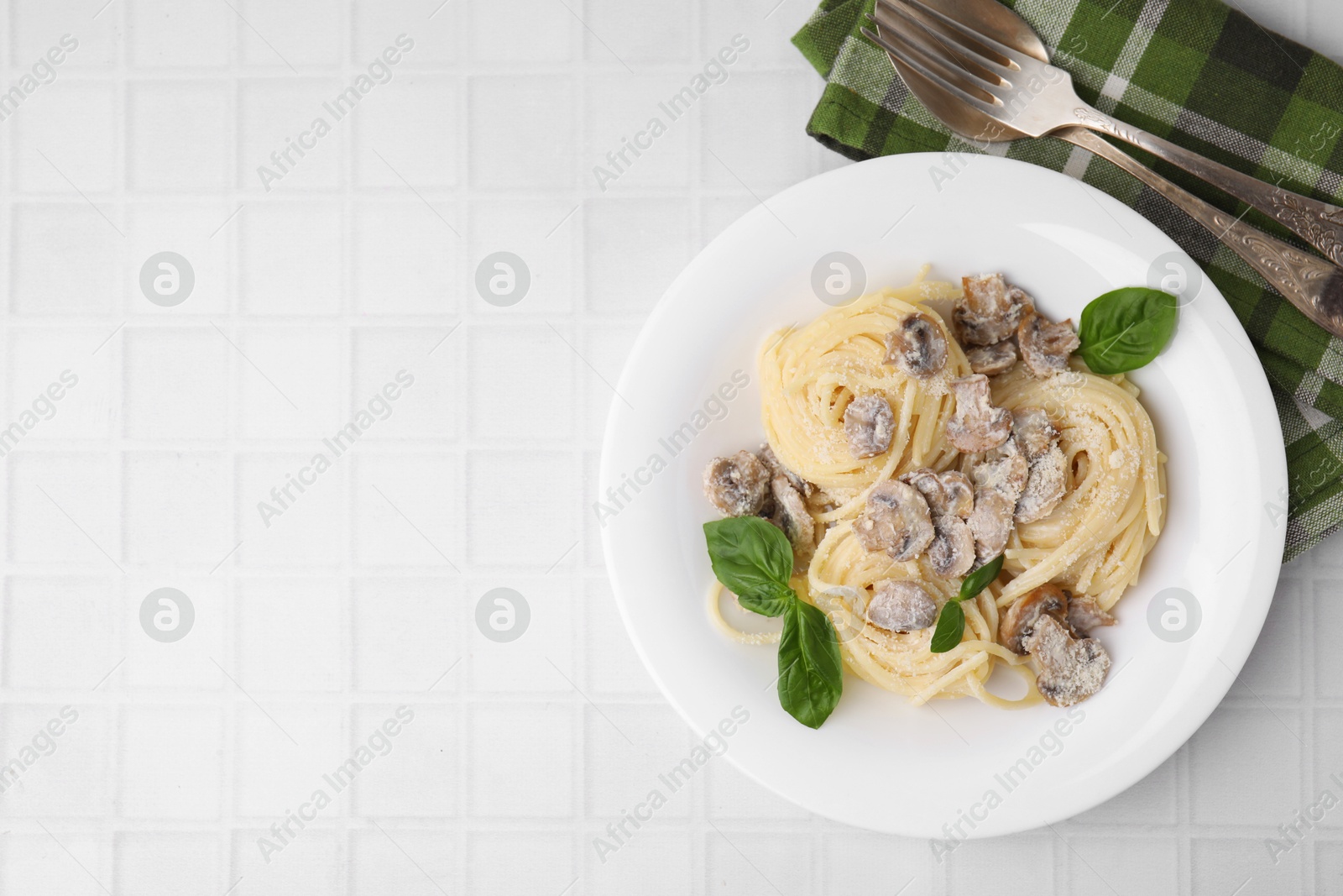 Photo of Delicious pasta with mushrooms and basil served on white tiled table, flat lay. Space for text