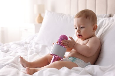 Cute little baby with microphone on bed at home, space for text