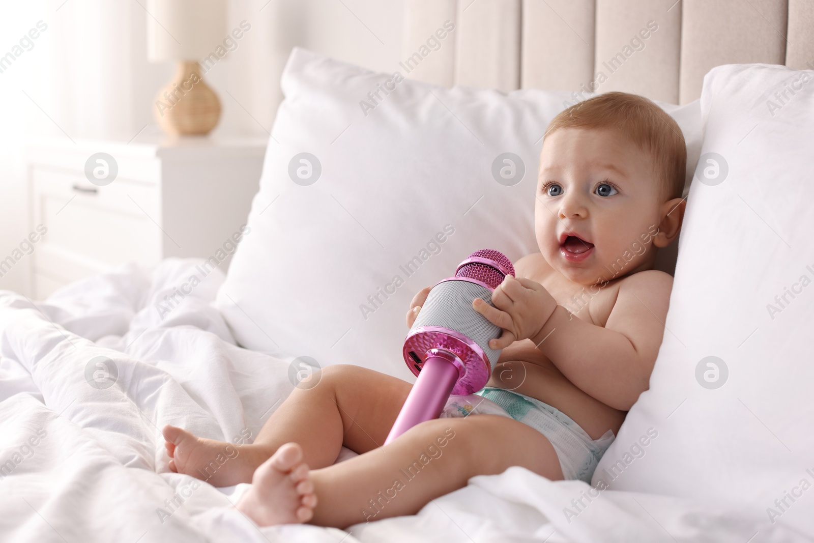 Photo of Cute little baby with microphone on bed at home, space for text