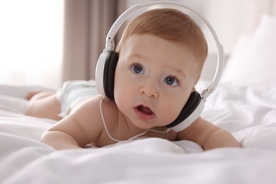 Photo of Cute little baby with headphones on bed at home