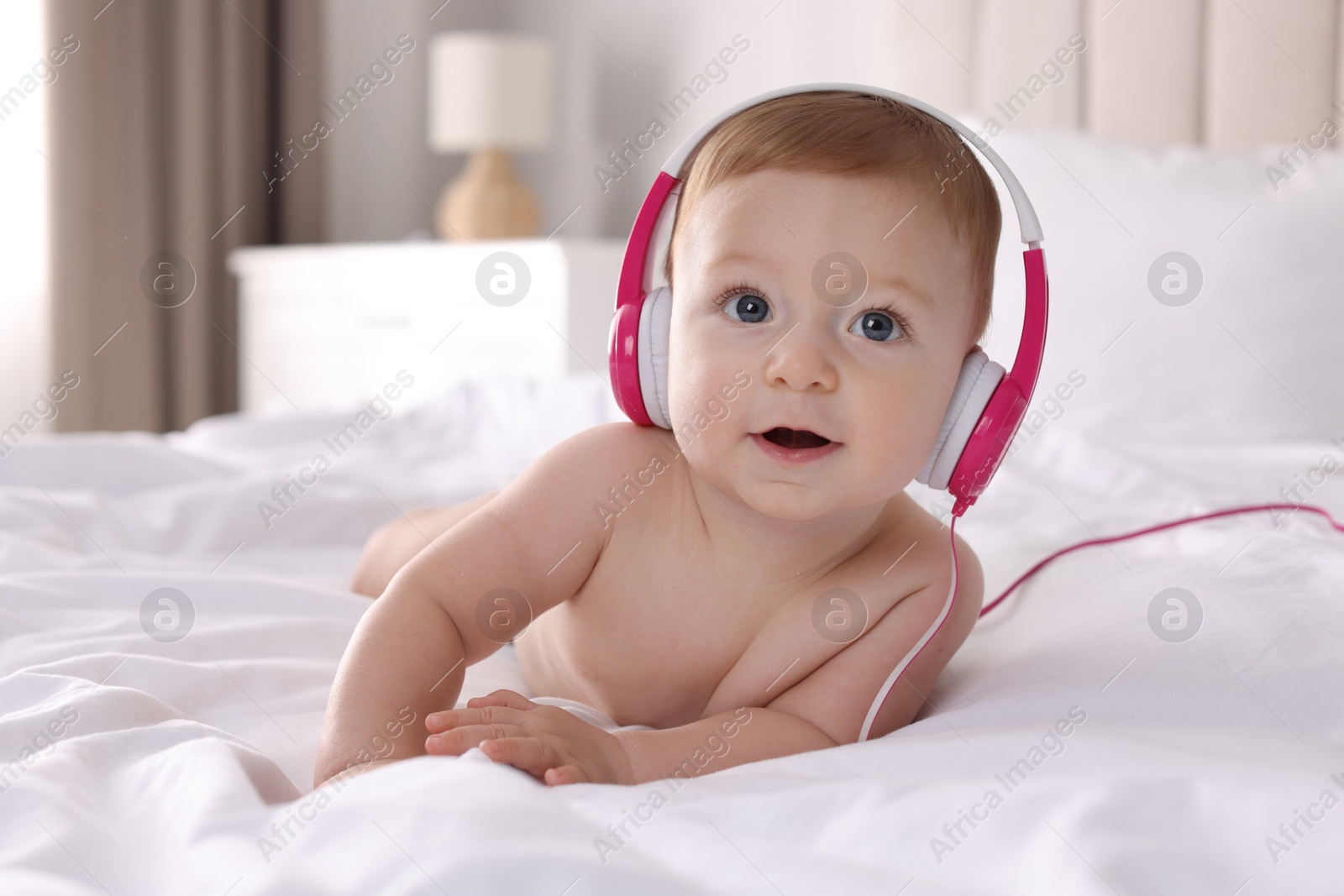 Photo of Cute little baby with headphones on bed at home