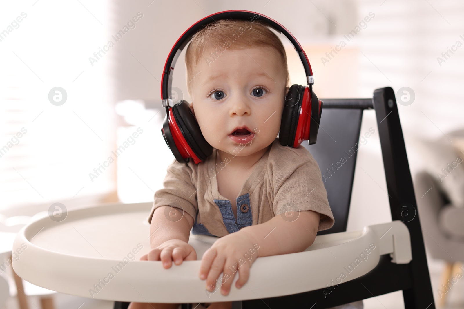 Photo of Cute little baby with headphones on high chair at home, space for text