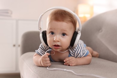 Cute little baby with headphones on sofa at home