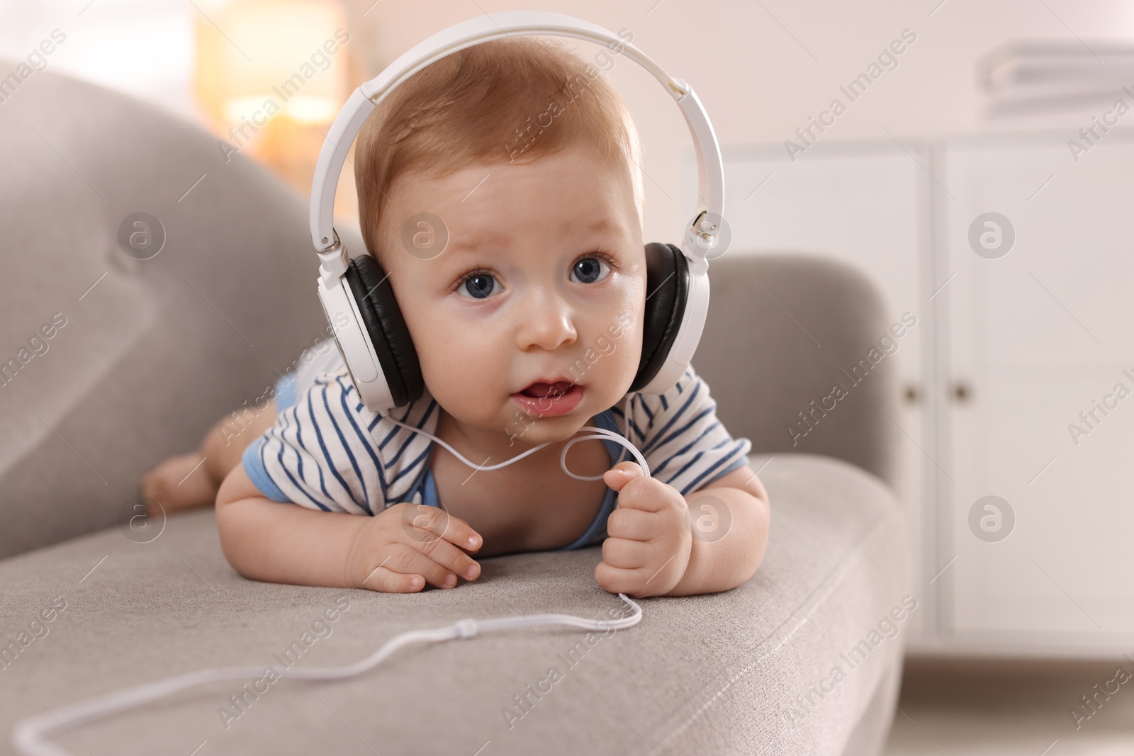 Photo of Cute little baby with headphones on sofa at home