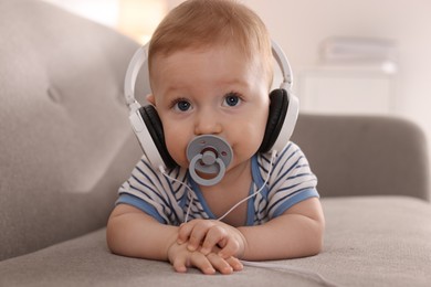 Cute little baby with headphones and pacifier on sofa at home