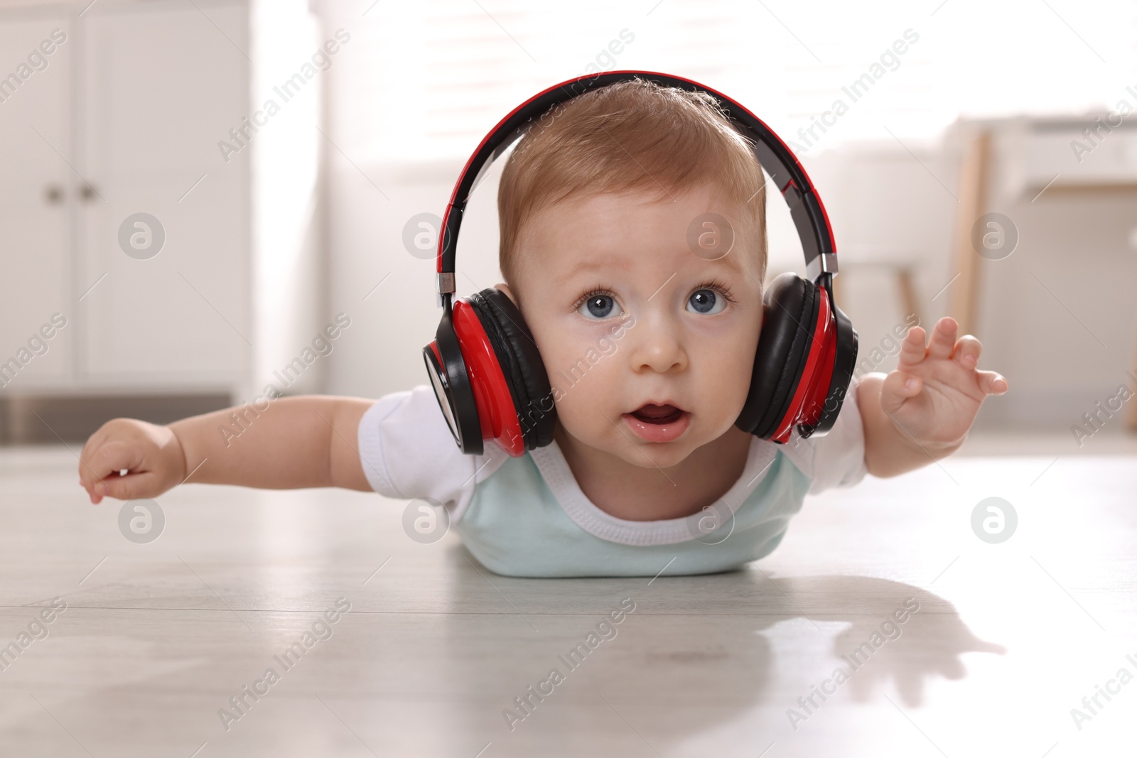 Photo of Cute little baby with headphones on floor at home